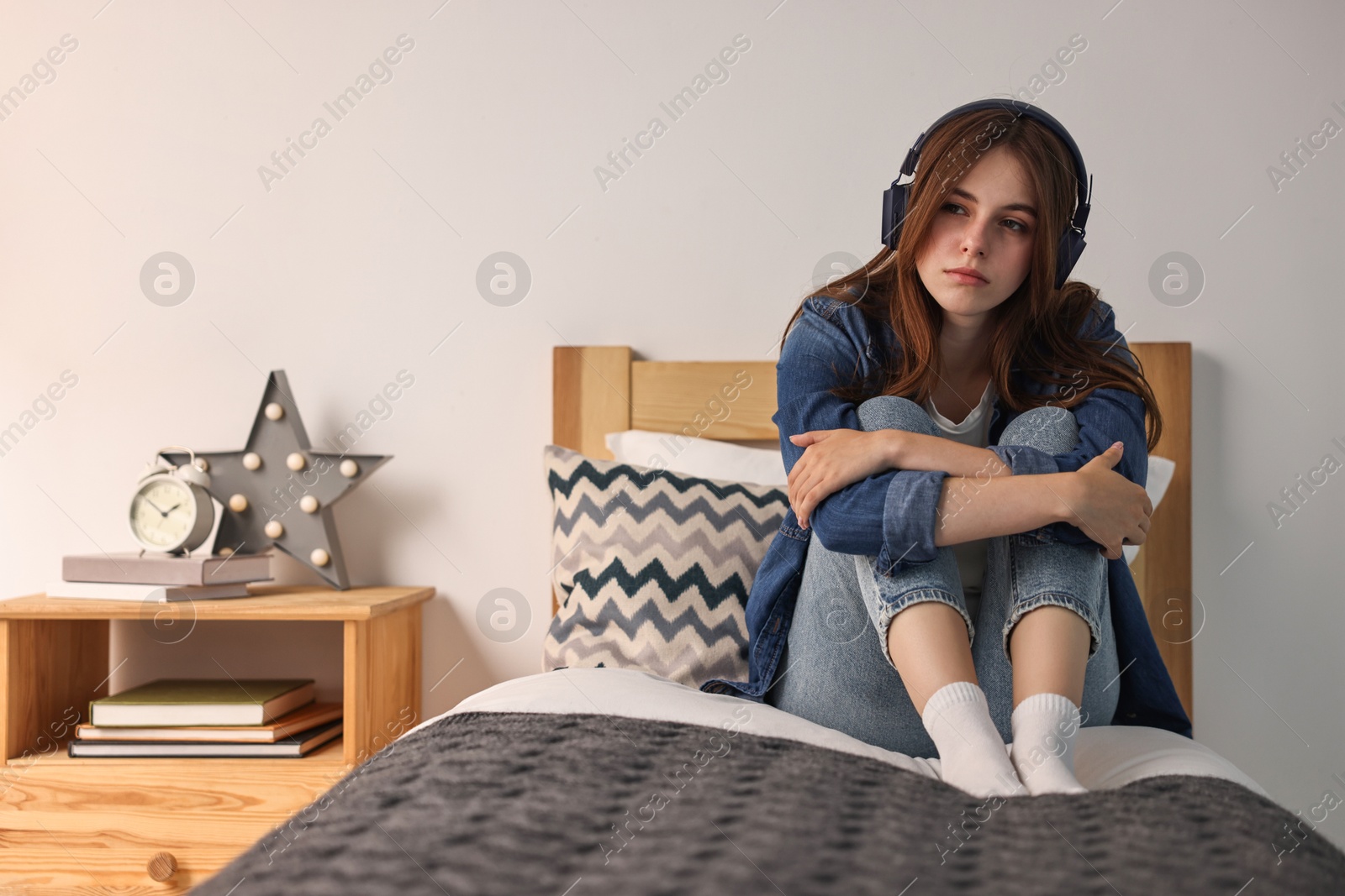 Photo of Loneliness concept. Sad teenage girl in headphones listening to music on bed at home