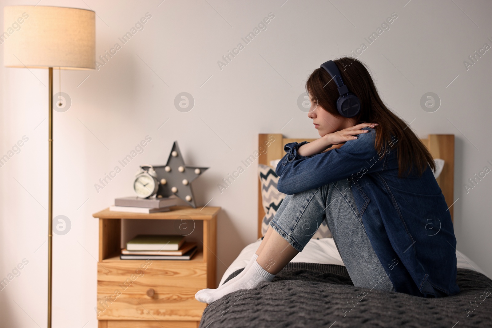 Photo of Loneliness concept. Sad teenage girl in headphones listening to music on bed at home