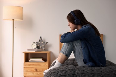 Photo of Loneliness concept. Sad teenage girl in headphones listening to music on bed at home