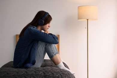 Photo of Loneliness concept. Sad teenage girl in headphones listening to music on bed at home