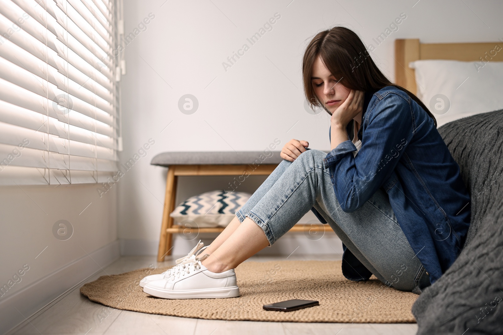 Photo of Loneliness concept. Sad teenage girl with smartphone on floor at home