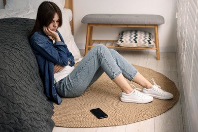 Loneliness concept. Sad teenage girl with smartphone on floor at home