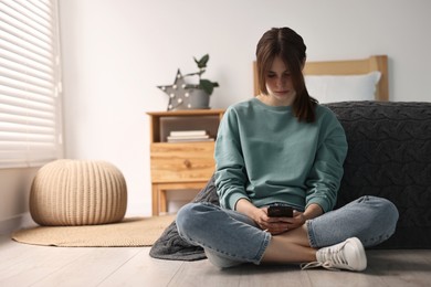 Loneliness concept. Sad teenage girl using smartphone on floor at home, space for text