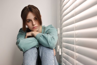 Loneliness concept. Sad teenage girl near window at home