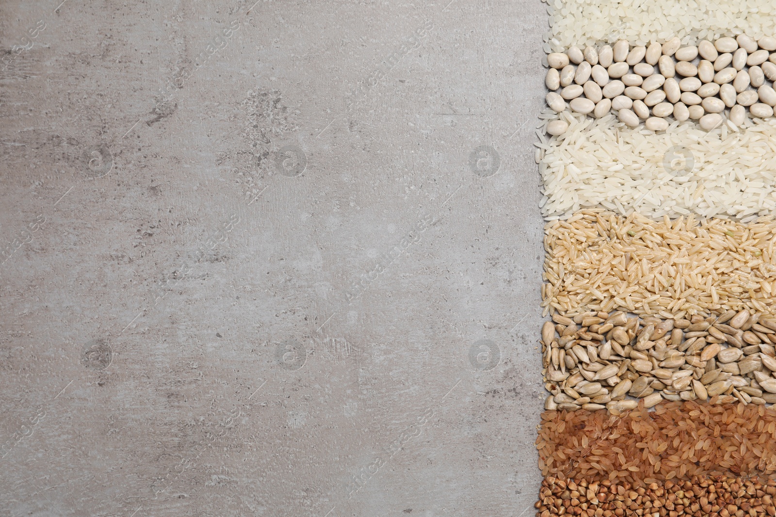 Photo of Different types of cereals, legumes and seeds on grey textured table, flat lay. Space for text