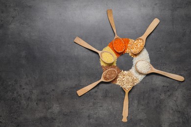 Photo of Different types of cereals and legumes in wooden spoons on grey table, flat lay. Space for text