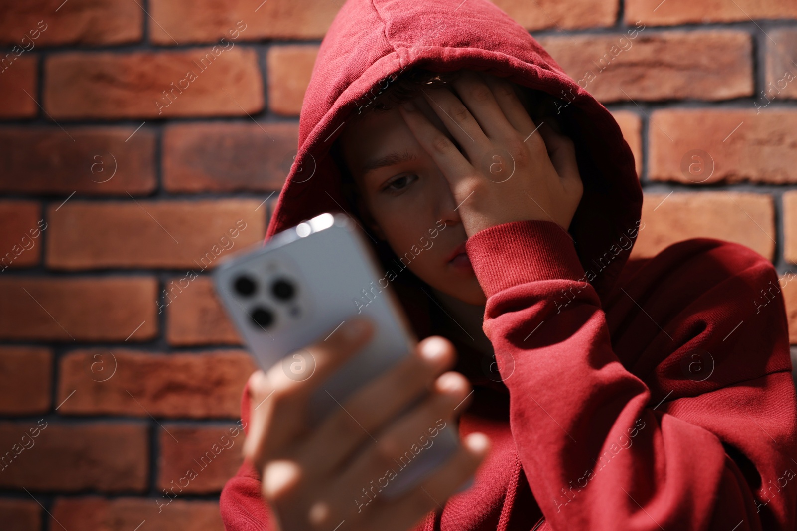 Photo of Loneliness concept. Sad teenage boy with smartphone near brick wall, selective focus