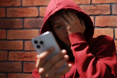 Loneliness concept. Sad teenage boy with smartphone near brick wall, selective focus