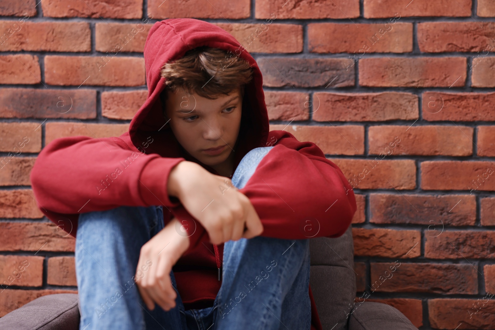 Photo of Loneliness concept. Sad teenage boy on armchair near brick wall