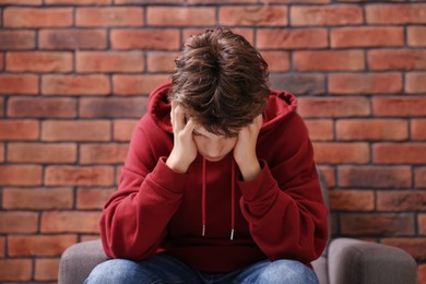 Loneliness concept. Sad teenage boy on armchair near brick wall