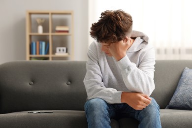 Loneliness concept. Sad teenage boy with smartphone on sofa at home