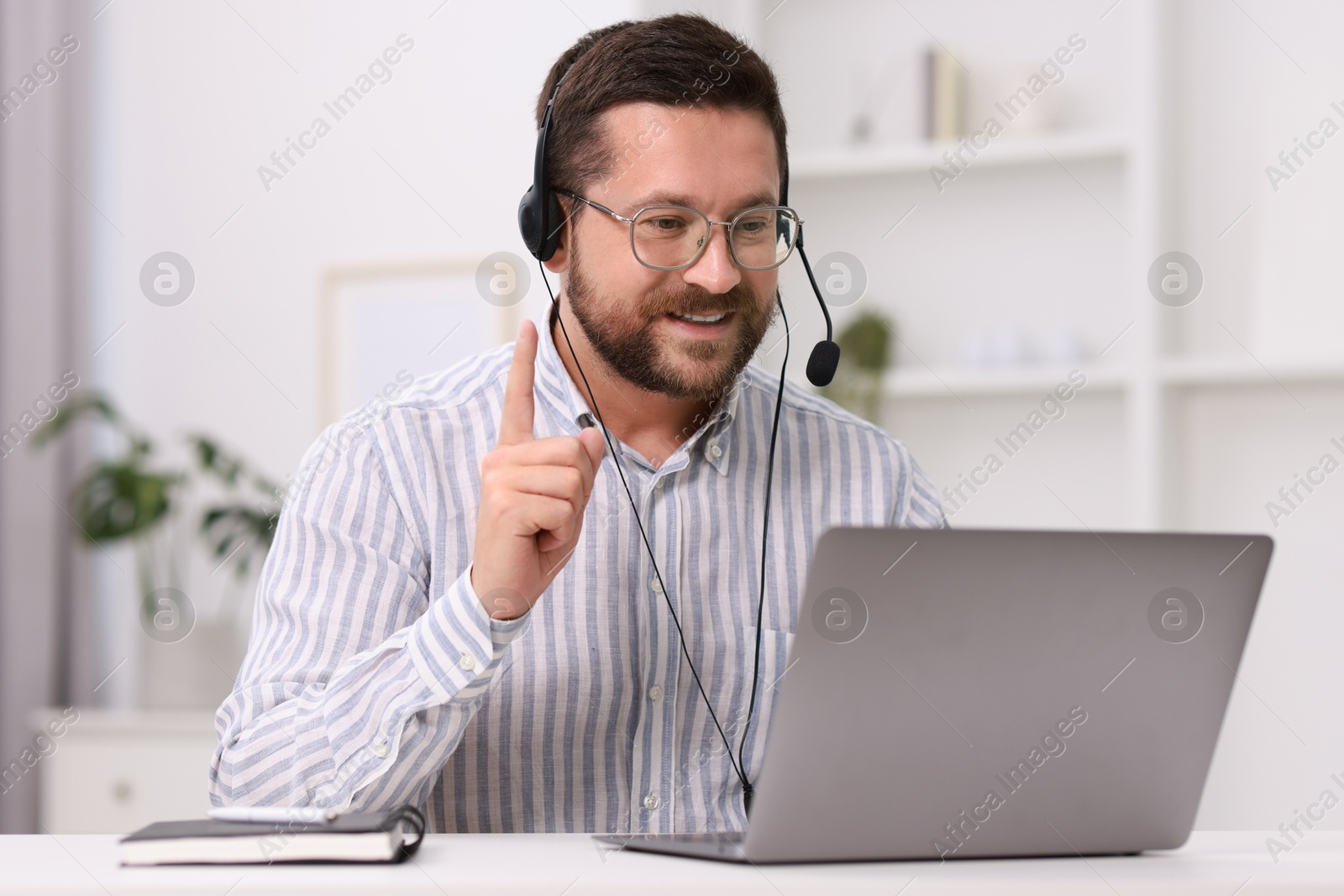 Photo of Interpreter in headset having video chat via laptop at white table indoors