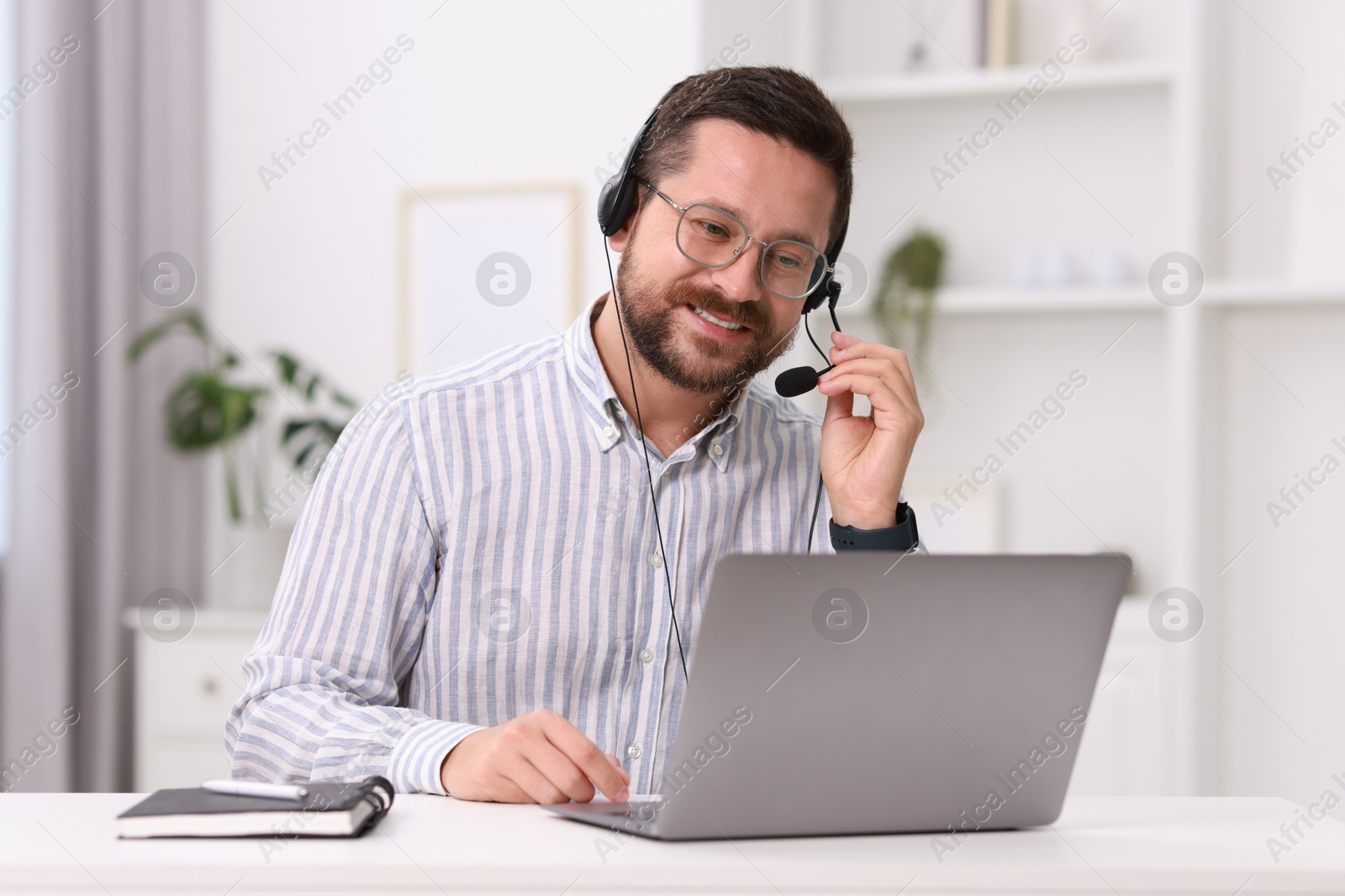 Photo of Interpreter in headset having video chat via laptop at white table indoors