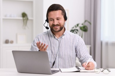 Interpreter in headset taking notes while having video chat via laptop at white table indoors