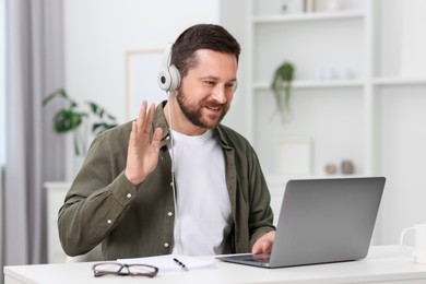 Interpreter in headphones having video chat via laptop at white table indoors