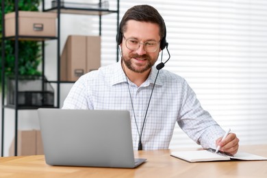 Photo of Interpreter in headset taking notes while having video chat via laptop at wooden table indoors