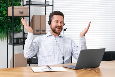 Photo of Interpreter in headset having video chat via laptop at wooden table indoors