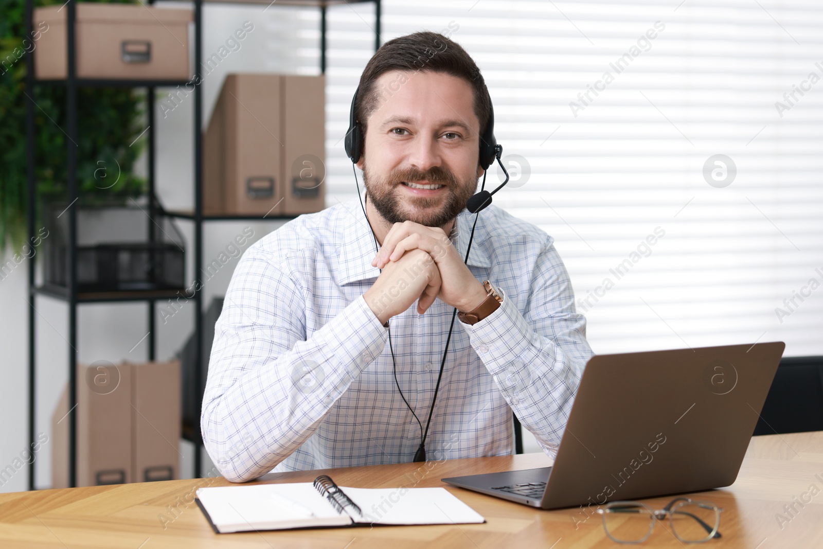 Photo of Interpreter in headset having video chat via laptop at wooden table indoors