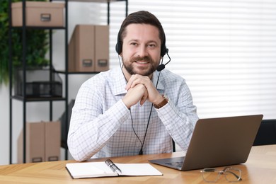 Photo of Interpreter in headset having video chat via laptop at wooden table indoors