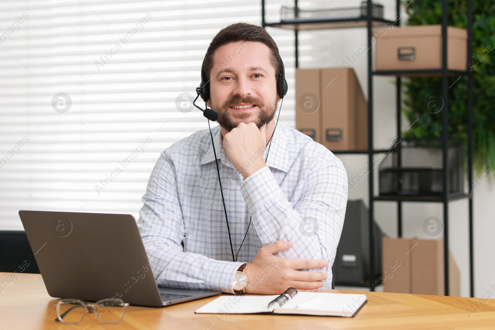 Photo of Interpreter in headset having video chat via laptop at wooden table indoors