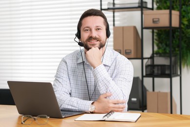 Interpreter in headset having video chat via laptop at wooden table indoors