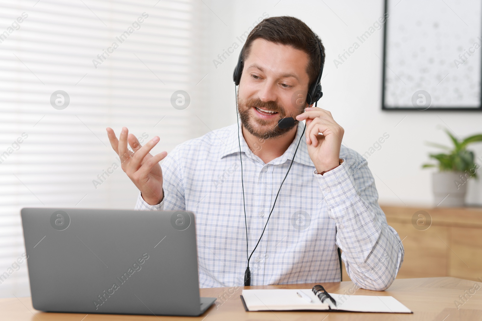 Photo of Interpreter in headset having video chat via laptop at wooden table indoors