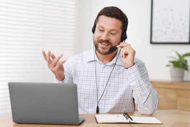 Interpreter in headset having video chat via laptop at wooden table indoors