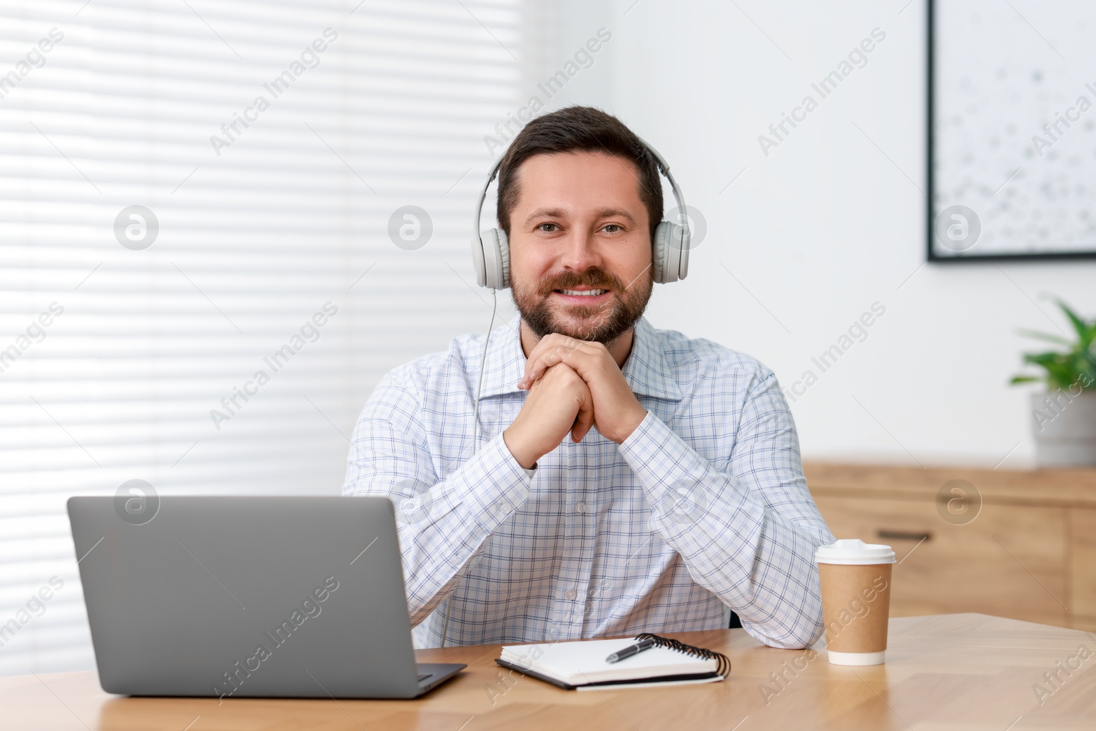 Photo of Interpreter in headphones having video chat via laptop at wooden table indoors