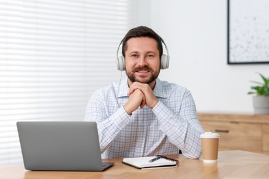 Interpreter in headphones having video chat via laptop at wooden table indoors