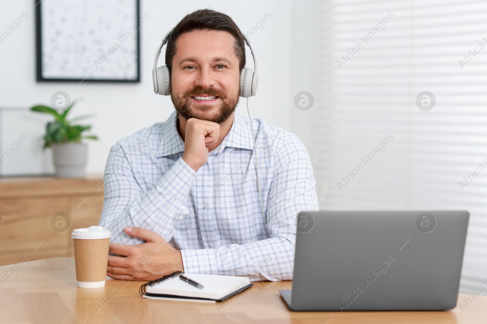 Photo of Interpreter in headphones having video chat via laptop at wooden table indoors