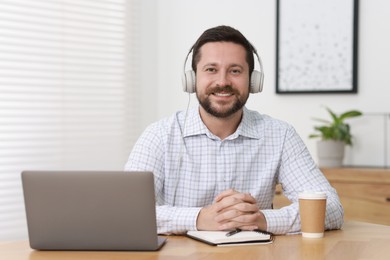 Interpreter in headphones having video chat via laptop at wooden table indoors