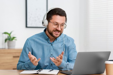 Interpreter in headphones having video chat via laptop at wooden table indoors