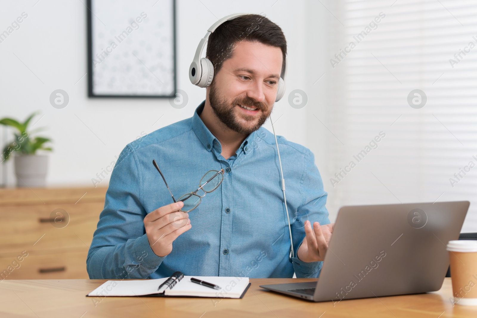 Photo of Interpreter in headphones having video chat via laptop at wooden table indoors