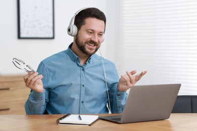 Interpreter in headphones having video chat via laptop at wooden table indoors