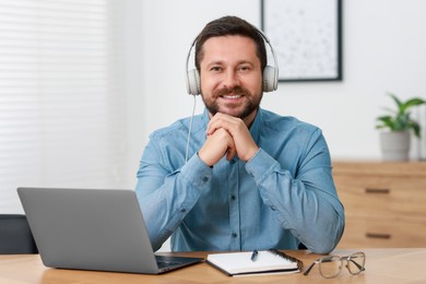 Photo of Interpreter in headphones having video chat via laptop at wooden table indoors