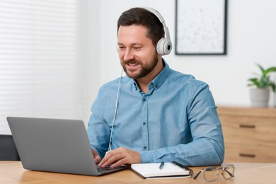 Photo of Interpreter in headphones having video chat via laptop at wooden table indoors