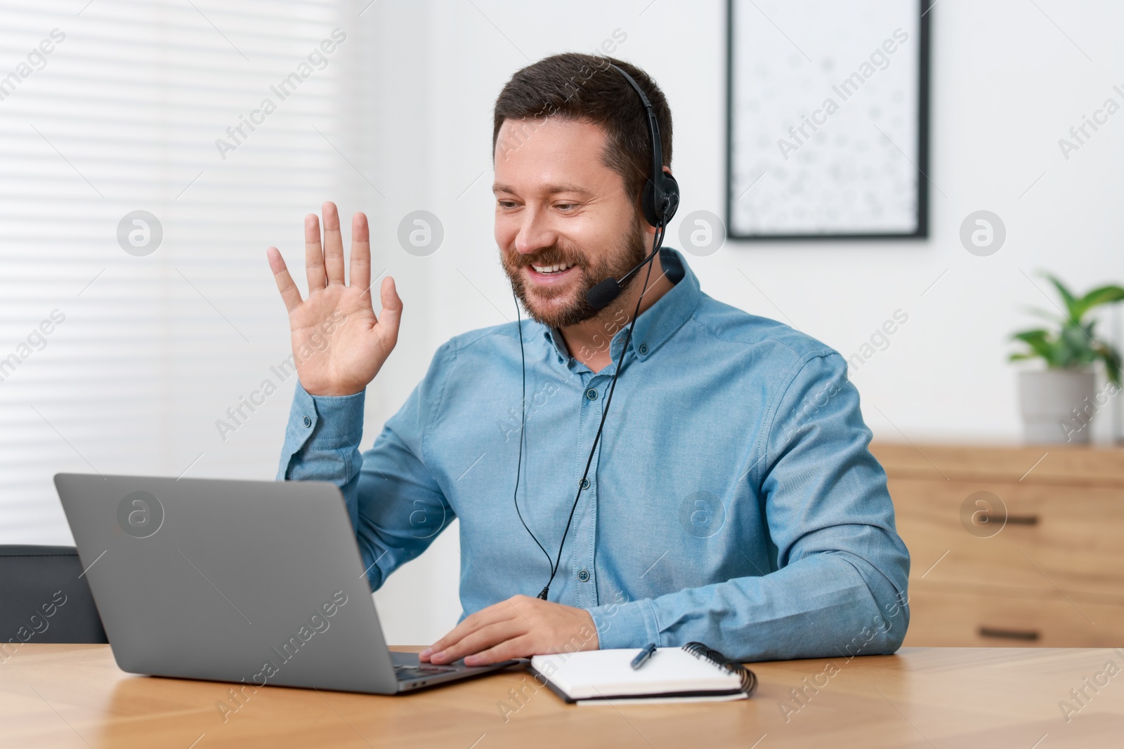 Photo of Interpreter in headset having video chat via laptop at wooden table indoors