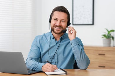 Photo of Interpreter in headset taking notes while having video chat via laptop at wooden table indoors