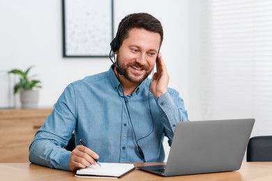 Interpreter in headset taking notes while having video chat via laptop at wooden table indoors