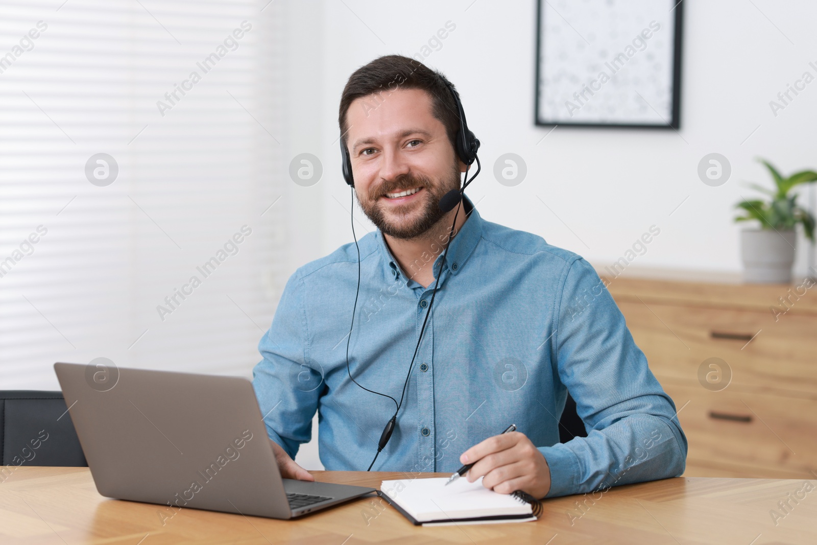 Photo of Interpreter in headset taking notes while having video chat via laptop at wooden table indoors