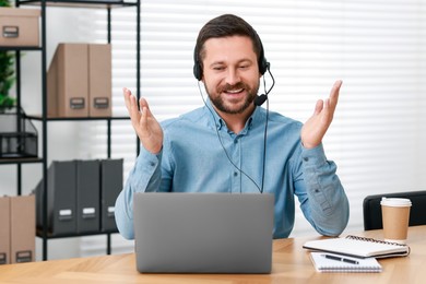 Interpreter in headset having video chat via laptop at wooden table indoors