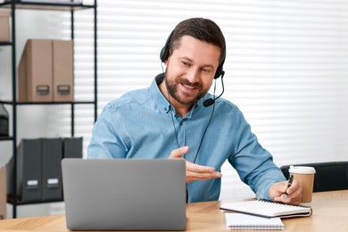 Interpreter in headset taking notes while having video chat via laptop at wooden table indoors