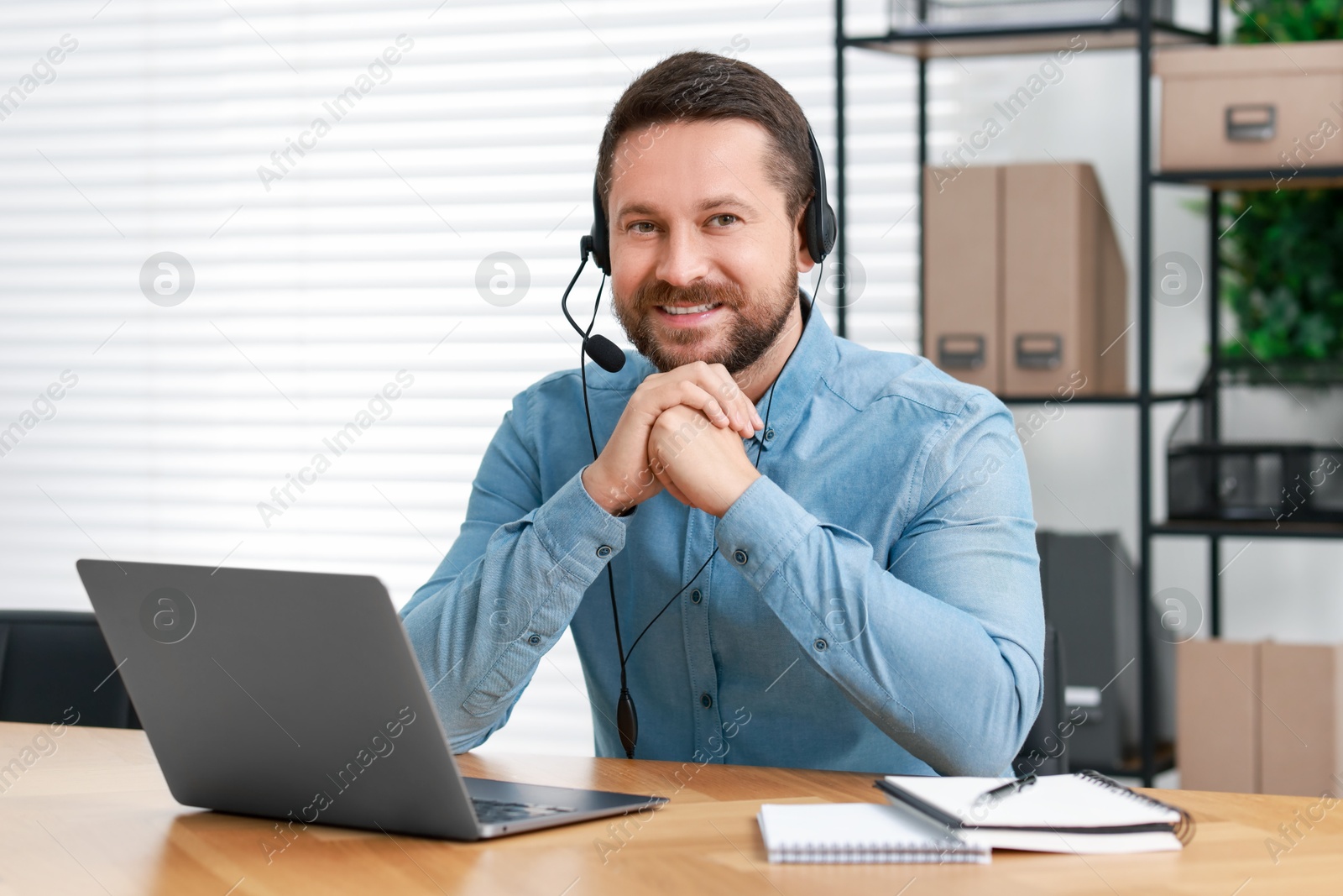 Photo of Interpreter in headset having video chat via laptop at wooden table indoors