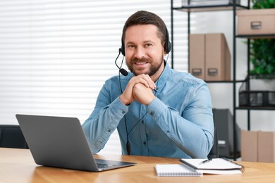 Interpreter in headset having video chat via laptop at wooden table indoors