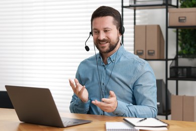 Interpreter in headset having video chat via laptop at wooden table indoors