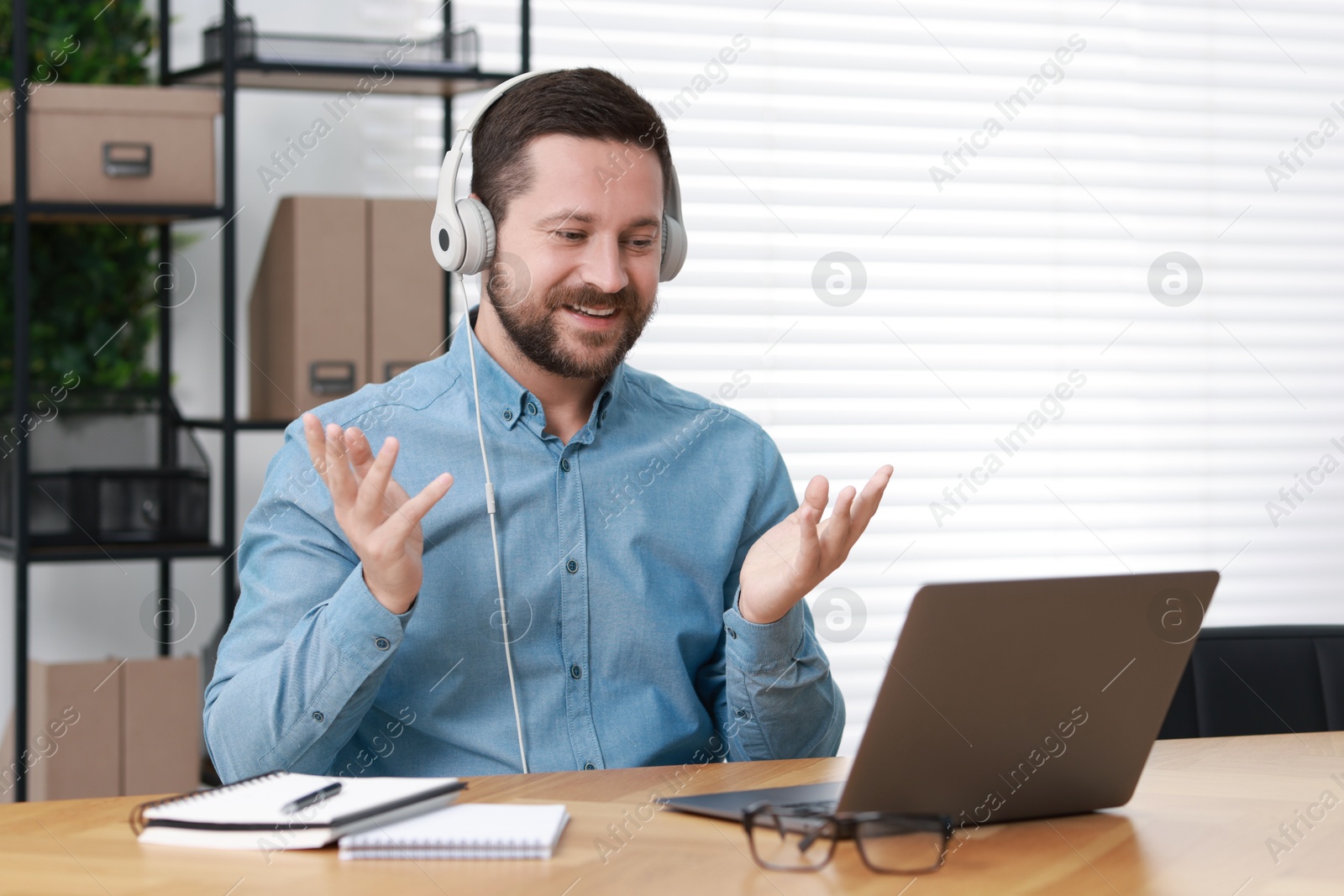 Photo of Interpreter in headphones having video chat via laptop at wooden table indoors