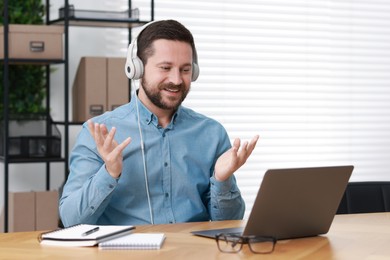 Interpreter in headphones having video chat via laptop at wooden table indoors