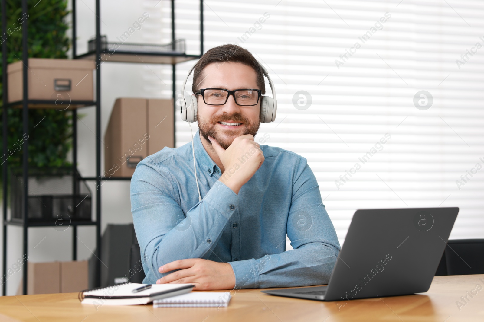 Photo of Interpreter in headphones having video chat via laptop at wooden table indoors