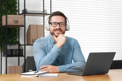 Photo of Interpreter in headphones having video chat via laptop at wooden table indoors