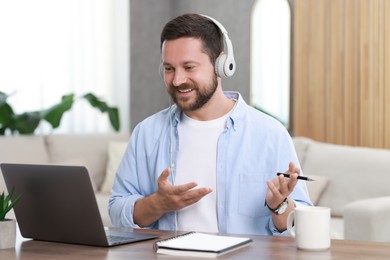 Interpreter in headphones having video chat via laptop at wooden table indoors